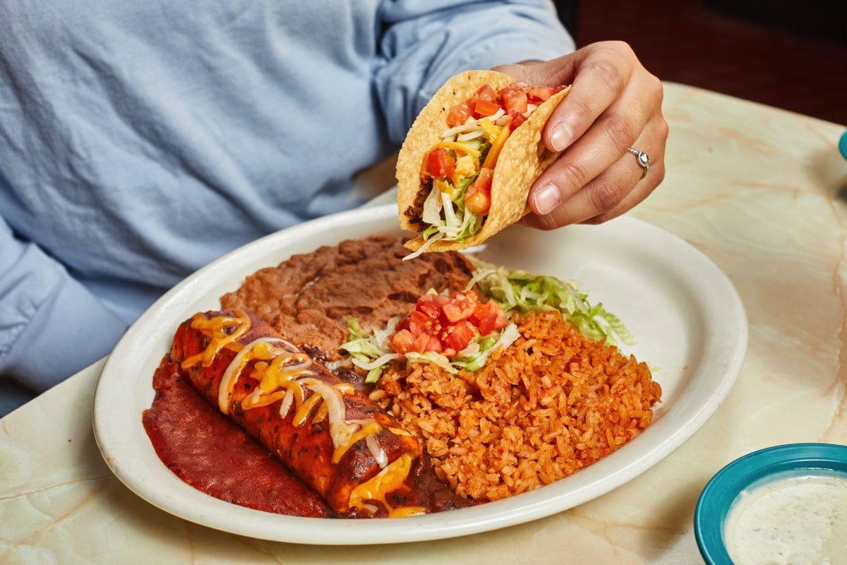 A person grabbing a taco off a plate of enchiladas