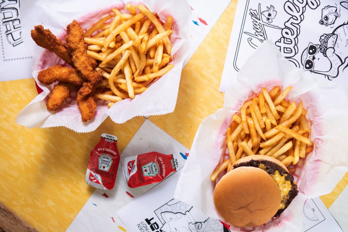 Basket of chicken tenders and french fries and a basket with a hamburger and fries, as well.